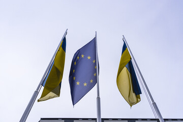 The flag of the European Union and two flags of Ukraine flutter in the wind in different directions...