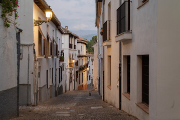 View of a narrow street with old floor and white historical buildings exterior in Granada, Spain