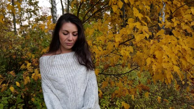 Portrait of a young brunette woman in a white sweater near autumn foliage in nature. Slow motion portrait. walking in nature.