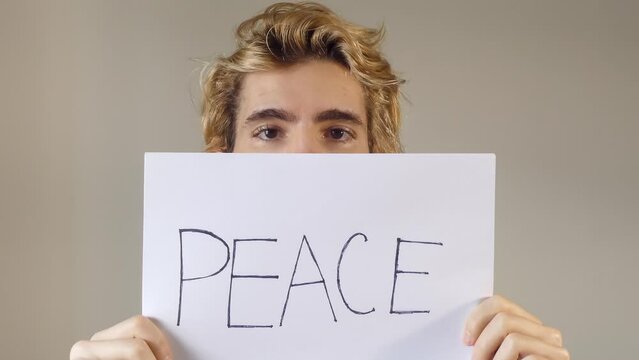 Adult Young Man Holding A Paper Message With The Text Peace, covering his face, a concept of peace 4k resolution