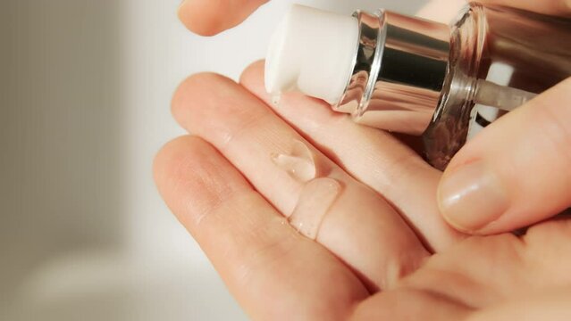 Push dispenser liquid facial fluid gel squeezed out to hand. Cosmetologist pours clear cleansing moisturizing hyaluronic serum acid. Cosmetic concept.