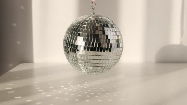 Disco ball rotates on a white background with shadows and casts rays of bright light. Glare and light reflection effect.