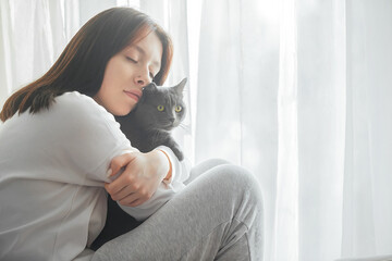 a beautiful young girl is dreaming about something, she hugged her gray cat and closed her eyes,...
