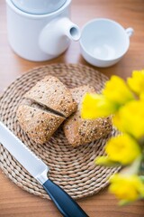 Still life of a kitchen table, dominated with bread, bread and knife, preparation of breakfast in full swing, in the background of yellow flowers and part of kettle or cup.