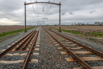 Endless looking straight railway tracks with catenary portals in a long row. The photo was taken near the Dutch city of Zevenbergen, Province of North Brabant.