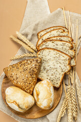 Freshly baked bread with wheat ears, buns, and toasts. Assorted bakery on light beige background