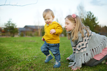 Fototapeta premium Big sister and her toddler brother having fun outdoors. Young girl playing with baby boy on spring day. Children with large age gap.