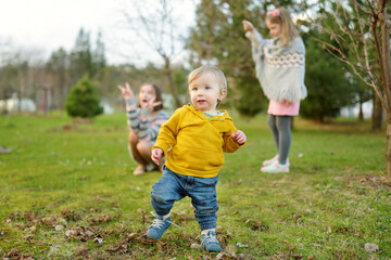 Fototapeta premium Two big sisters and their toddler brother having fun outdoors. Two young girls and a baby boy on summer day. Children with large age gap. Big age difference between siblings.