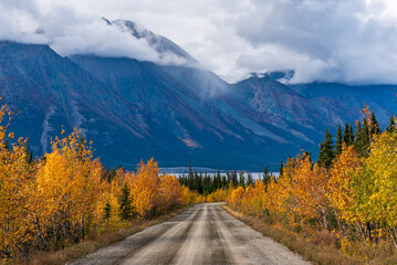 Dirt road headed to  mountain landscape in northern Canada during September, fall season with...