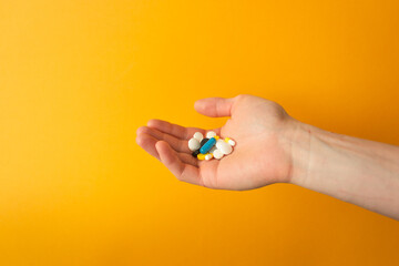 Man's palm holds a handful of different multicolored pills, capsules and drops. Yellow background. Health care concept.