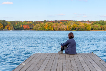 Woman sitting on a wooden jetty on a lake on a sunny autumn day. Concept of meditation.