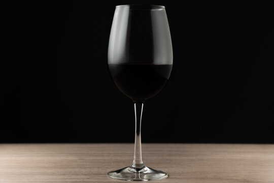 horizontal photo of glass of red wine in the center of a wooden table with a black background