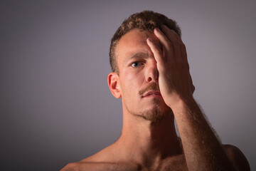 A shirtless boy covers half of his face and looks towards the camera. Thoughtful and spiritual man