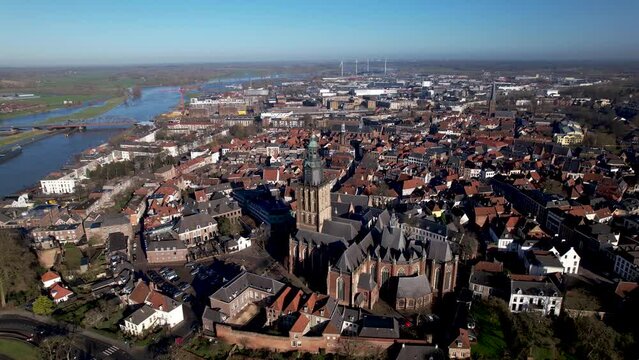 Aerial approach of picturesque medieval city wall of tower town Zutphen with authentic historic rooftops and buildings with Walburgiskerk church towering over against a clear blue sky.