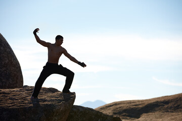 Kickboxing on the mountain. A male athlete kickboxing on the edge of a cliff on a mountain.