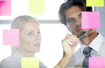 Reflecting on our teams success. A man and woman in the office looking at notes on a glass window,...