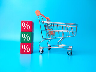 Shopping chart and wooden block with persentage symbol on blue background.