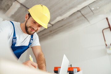 Cheerful repairman writing down details of an order while standing indoors during renovation work
