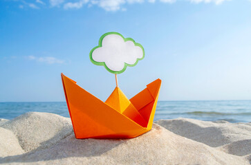 Orange Paper Boat on Sandy Seashore Close-up. Small Paper Boat on Background of Blue Sea on Sunny Summer day. Stick with empty white blank speech bubble in Boat. Concept Travel, Tourism, Vacation Rest