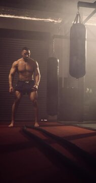 A Vertical Video Of A Hispanic Bodybuilder Exercising Battle Ropes In An MMA Gym. Shot In A Crossfit Boxing Gym With Low Key Lighting And A Scattering Of Haze. Captured On Red Digital Cinema Camera 