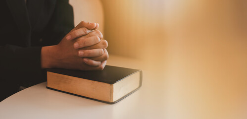 A Woman Hands folded in prayer on a Holy Bible in church concept for faith, spirituality and...