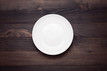 Empty ceramic white plate on brown wooden table background / Copy space Top view