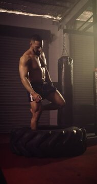 A Vertical Video Of A Hispanic Bodybuilder Doing A Tyre Walk In An MMA Gym. Shot In A Crossfit Boxing Gym With Low Key Lighting And A Scattering Of Haze. Captured On Red Digital Cinema Camera 