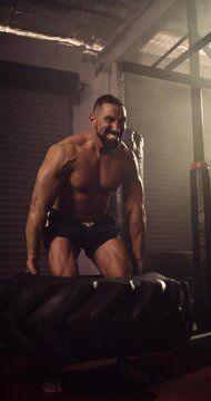 A Vertical Video Of A Hispanic Bodybuilder Exercising, Farmer Tyre Walk In A Gym. Shot In A Crossfit Boxing Gym With Low Key Lighting And A Scattering Of Haze. Captured On Red Digital Cinema Camera 