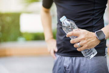 Active Asian sportsman relaxing and drinking a water in bottle after outdoor running or workout.