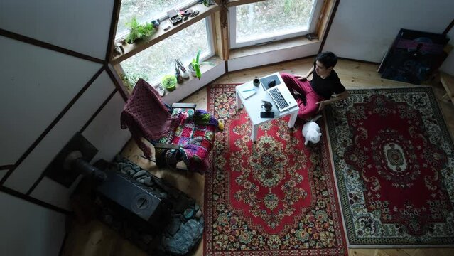 Young man working and relaxing with laptop in vintage style geo dome. Vintage carpet on the floor, rocking chair, paintings on the walls