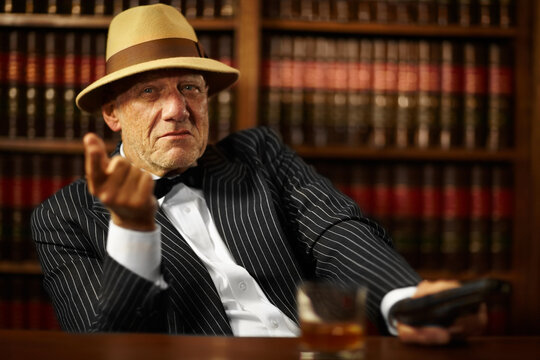 He heads up a large criminal organisation. Aged mob boss wearing a hat and looking serious while pointing.
