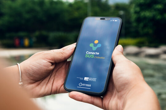 Girl in the park holding a smartphone with Conecte SUS (Brazil health app to check vaccination) app on the screen. Green area and an artificial lake. Rio de Janeiro, RJ, Brazil. February 2022