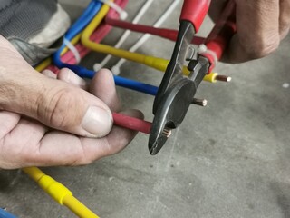 An electrical technician cutting insulated wire using cable cutter.