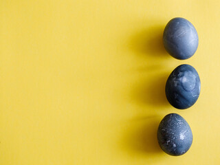 Three black eggs handmade painted by hibiscus tea on yellow background. Design, visual art, minimalism Flat lay top view, copy space. Happy Easter monochrome concept Aesthetic look. Contemporary style