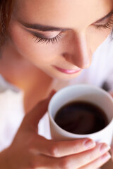 Starting her day with a fresh cup of coffee. A young woman looking thoughtful while drinking her morning coffee.