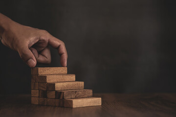 Close-up hand is placing wood block tower stacked in pyramid stair step with caution to prevent...