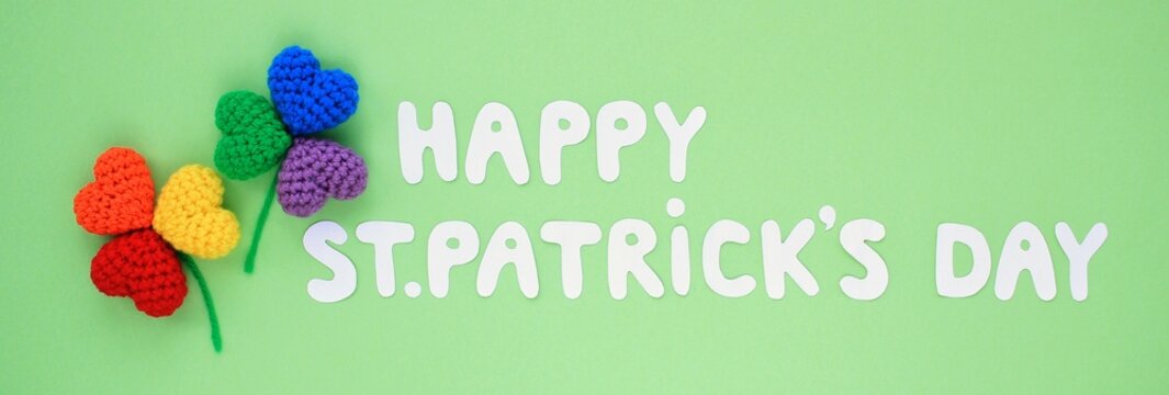 Happy St. Patrick's Day banner lettering with two rainbow lgbt shamrock leaves on green background. Creative minimalistic lay out concept. 