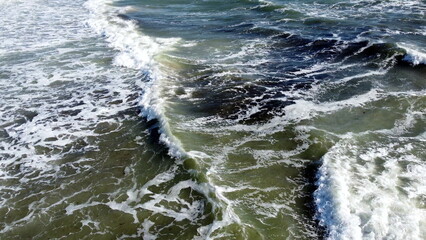 Aerial drone view flight over sea waves that roll onto sandy shore. Top view. Waves with white foam hit sandy shore. Nature, natural background. Concept eco, environment, climate change, traveling