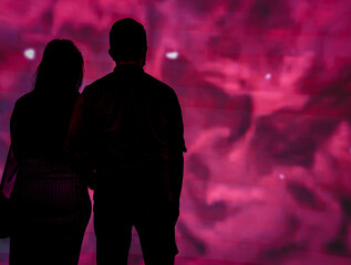 silhouettes of people looking at brightly lit pink coloured screen