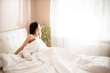 Morning. A young brunette woman wakes up in her bed by the window. Sunlight. Lifestyle