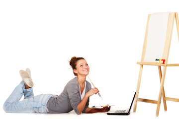 Im looking everywhere for inspiration. Shot of smiling young woman lying down by her laptop and a blank canvas on an easel. © Andrei Z/peopleimages.com