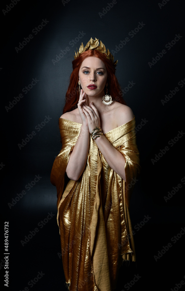 Poster  Full length portrait of pretty female model wearing  grecian goddess  toga gown, posing with elegant gestural movements on a studio background.