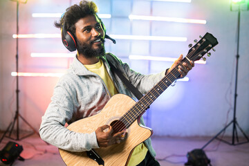 Professional young music artist playing guitar by singing on stage with neon ligt background -...