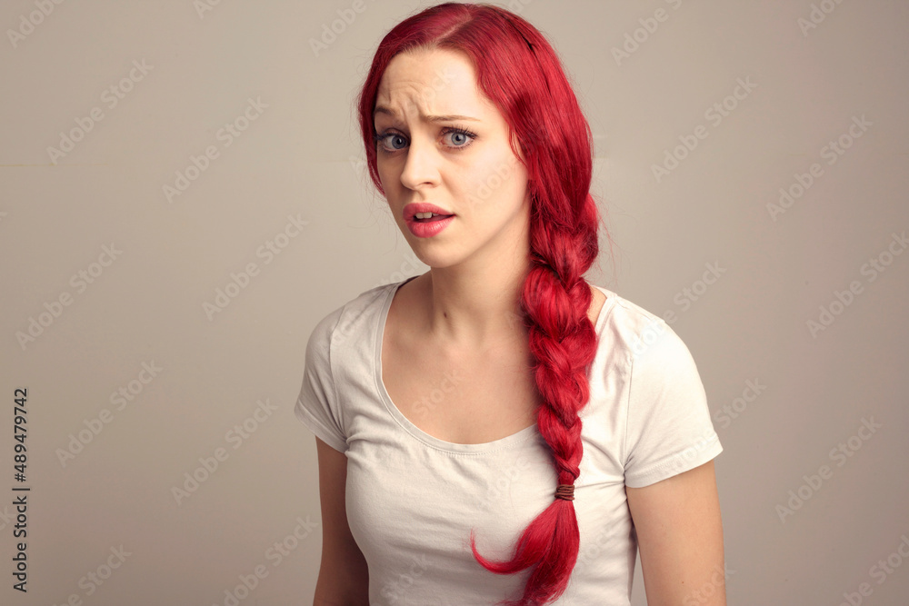 Wall mural close up portrait of pretty female model with red hair in a braid, expressing emotion over the top facial expression on a studio background.