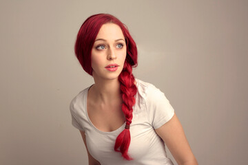 close up portrait of pretty female model with red hair in a braid, expressing emotion over the top facial expression on a studio background.