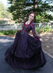 Full length portrait of red-haired woman wearing a historical victorian gown costume, walking around beautiful location with  Gothic stone architecture.