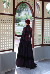 Full length portrait of red-haired woman wearing a historical victorian gown costume, walking...