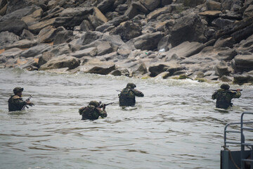 Four soldiers in military uniforms come out of the water to the shore with a rifle over their heads. War games or military exercises. 