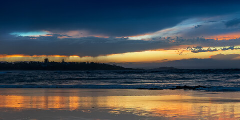 Scenic sunset on the ocean sandy beach with town silhouette on the horizon. Beautiful view landscape background. Australia