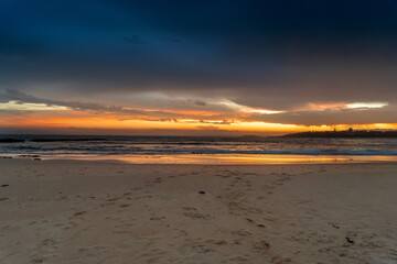 Scenic sunset on the ocean sandy beach with town silhouette on the horizon. Beautiful view landscape travel background. foorptints on sand.